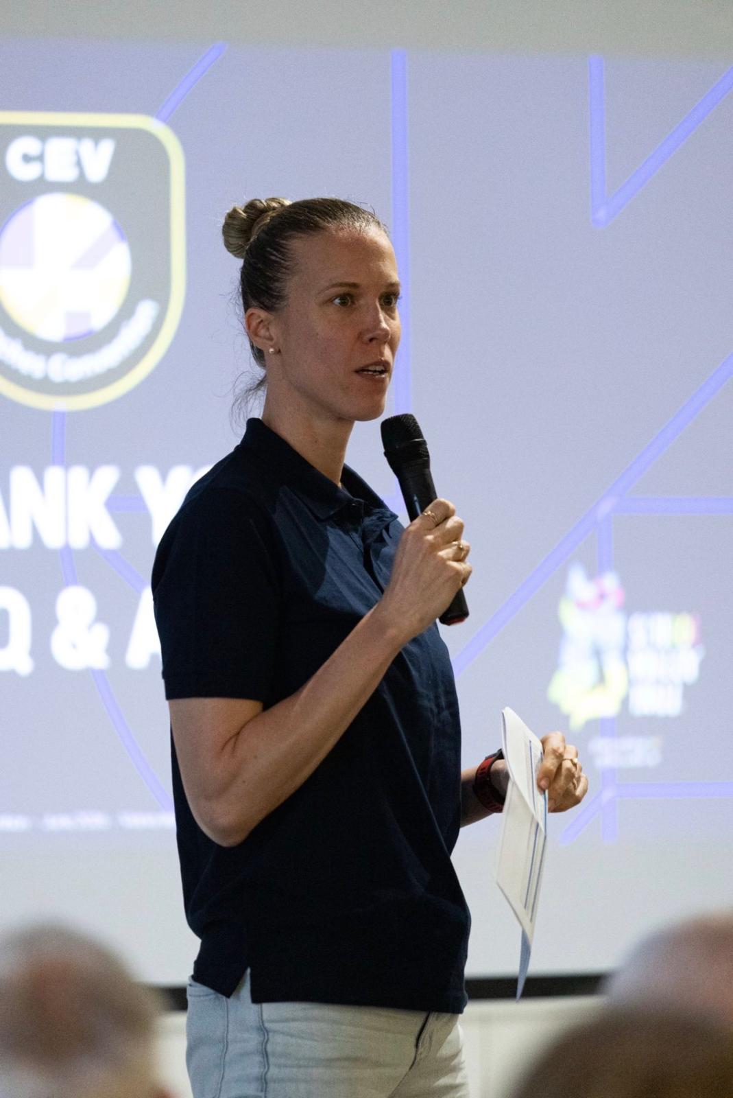 Jana Kulan speaking into a microphone at a volleyball event
